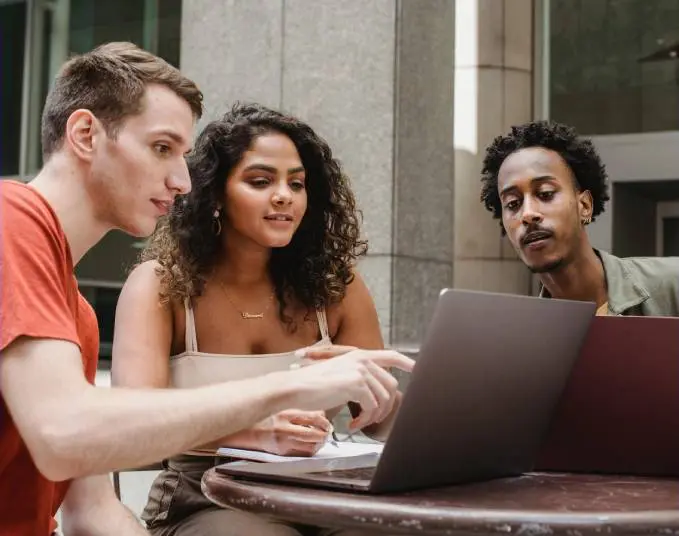 Three people sitting at a table looking at a laptop.