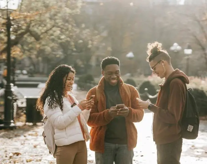 Three people standing outside looking at a phone.